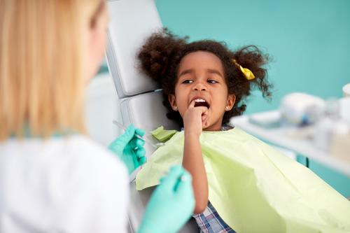 photo of a young girl sitting in the dentist chair pointing to a tooth