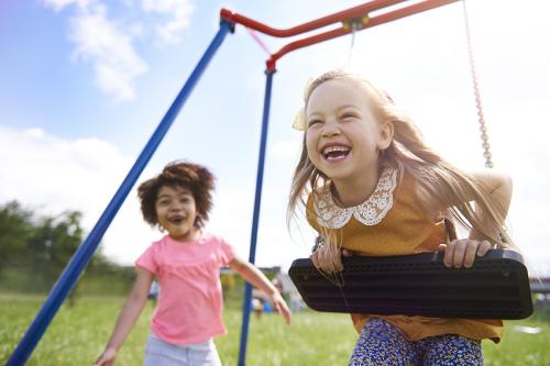 stock photo of two little girls laughing and playing on a play set outside